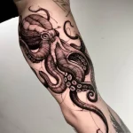 Фото тату: стилизованный осьминог, выполненный в технике blackwork, на руке. Детализированные щупальца и выразительные глаза.