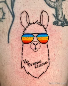 Фото тату ламы в очках с радужной оправой и с надписью "No Drama Llama". Рисунок выполнен в ярком и позитивном стиле.