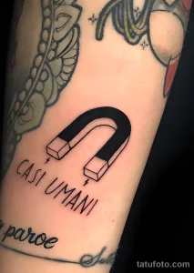 Фото тату: минималистичная татуировка магнита подковообразной формы с надписью "CASI UMANI" на руке.