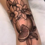 Фото тату: черно-белая татуировка апельсина с цветами в стиле blackwork на руке. Детализированная проработка теней и узоров.