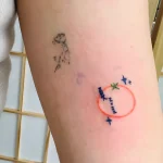 Фото тату: минималистичный рисунок бумажного самолетика в красном круге с облаками и надписью на боку. Необычный и креативный дизайн.
