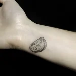 Фото минималистичной татуировки на запястье с изображением ломтика апельсина, выполненной в технике лайнарт.