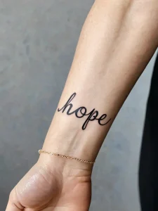Фото татуировки с надписью 'Hope' на запястье, выполненной изящным рукописным шрифтом. Символизирует надежду и оптимизм.