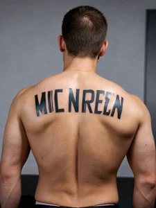 Фото тату: черная текстовая татуировка с именем 'MIC NREEM' на спине мужчины, выполненная крупным шрифтом.