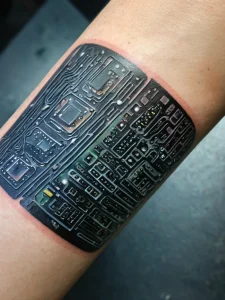 Фото тату: реалистичное изображение печатной платы с микросхемами и дорожками, выполненное на руке в черно-серых тонах. Футуристический рисунок татуировки.