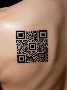 Фото тату: минималистичный QR-код, нанесенный на плечо человека, выполненный в черном цвете.