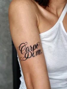 Фото тату: надпись "Carpe Diem" красивым каллиграфическим шрифтом. Черно-белая татуировка на руке.