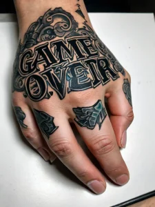 Фотография татуировки с надписью 'GAME OVER' в стильном шрифте на руке человека, с элементами игрового дизайна.