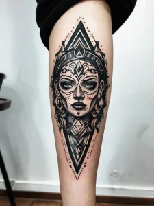 Фото тату в стиле Blackwork с изображением лица, окруженного геометрическими узорами. Детализированный рисунок на бедре.