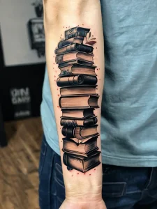 Фото реалистичной татуировки на руке, изображающей стопку старинных книг. Детализированный рисунок с переплетами, страницами и потертостями.