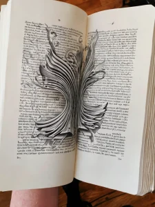Черно-белая татуировка старинной книги с пером на развороте. Детализированный рисунок с реалистичными страницами, переплетом и декоративными элементами.