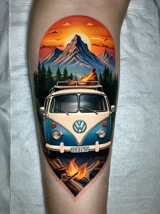 Фото тату: реалистичный рисунок Volkswagen Bus на ноге с изображением костра и горного пейзажа на фоне заката.