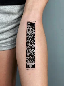Фото татуировки в виде QR-кода на икре ноги, выполненной в черном цвете с надписью.