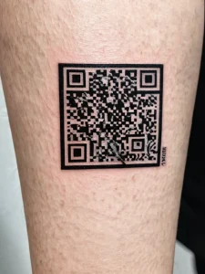 Фото татуировки в виде QR-кода на руке человека, выполненной в черном цвете.
