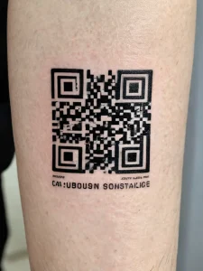 Фото татуировки в виде QR-кода на ноге человека, выполненной в черном цвете.