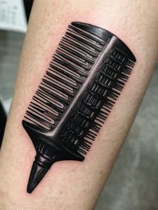 Фото тату: изображение расчески, выполненное в стиле blackwork. Минималистичный рисунок, подчеркивающий форму и текстуру предмета.