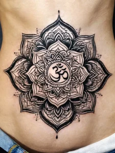 Фото тату символа Ом в центре цветка лотоса, выполненного в технике blackwork на животе. Детализированный рисунок с тонкими линиями и точками.