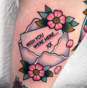 Фото тату на руке: красочная открытка с надписью 'Wish You Were Here' и розовыми цветами в стиле олд скул.