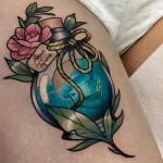 Фото тату на предплечье: череп в прозрачной бутылке, украшенной розовыми цветами и голубой лентой. Яркий и детализированный рисунок татуировки.