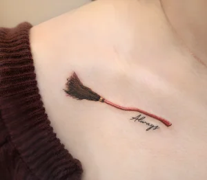 Фото тату на ключице с изображением метлы и надписью 'Always'. Татуировка выполнена в черно-белой гамме с использованием тонких линий.