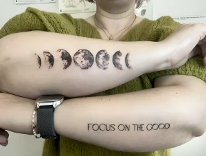 Фото тату: минималистичная татуировка фаз луны и надпись 'FOCUS ON THE GOOD' на предплечье. Вдохновляющий и стильный дизайн.