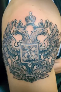 Фото татуировки на руке, выполненной в технике blackwork, изображающей двуглавого орла с детально проработанными перьями и тенями. Использованы только черные чернила.