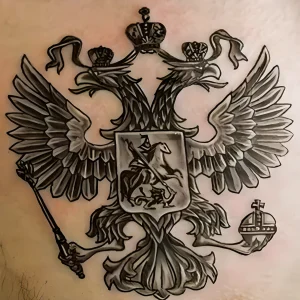 Фото реалистичной татуировки на груди, изображающей двуглавого орла с детально проработанными перьями и тенями. Использованы оттенки серого и черного.