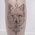 Фото татуировки головы лисы в стиле blackwork с добавлением цветочных элементов. Элегантный и минималистичный рисунок татуировки на ноге.