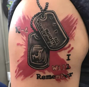 Фото тату на плече: армейские жетоны, брызги крови и надпись 'I Will Remember'. Черно-красный рисунок татуировки.