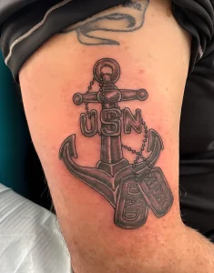Фото тату якоря с надписью USN и жетонами с гравировкой 'DAD' и 'HERO'. Черно-серый рисунок на предплечье, символизирующий морскую службу и отцовство.