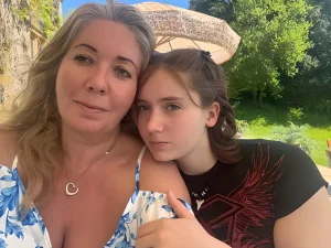 Мать и дочь, обнимающиеся на фоне тропического пейзажа. Дочь с татуировкой на плече.