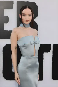 Dove Cameron позирует на красной дорожке в светло-голубом атласном платье с вырезом и чокером, видны татуировки на руке.