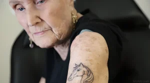 Крупный план Жанны Робинсон, 91-летней женщины, демонстрирующей новую татуировку в виде головы лошади на плече.