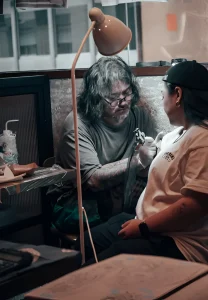 Тату-мастер работает над татуировкой на руке клиента во время мероприятия CENSU Crew Tattoo Pop-Up в Golden Gip.