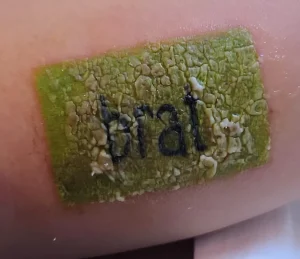 Крупный план сильно воспаленной татуировки с надписью 'brat' на коже.