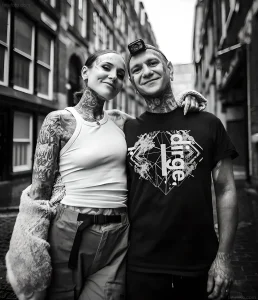 Модели с татуировками Monami Frost и мужчина на фоне кирпичной стены, черно-белое фото.
