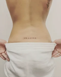 Минималистичная татуировка надписи "IMAGINE" на пояснице