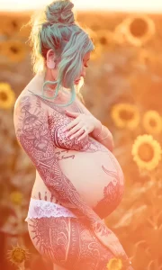 Татуированная модель Summer McInerney на фоне поля подсолнухов, демонстрирующая татуировки в стиле неотрадишнл на спине и боку.