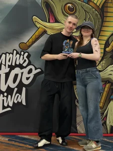 Фото тату-мастера Ильи Кузнецова на Memphis Tattoo Fest с девушкой и его работами на руке модели.