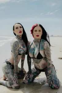 Makani Terror, тату-модель с масштабными татуировками в стиле цветного реализма, на фоне пляжа.
