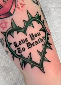 Фото татуировки: сердце, обвитое шипами, с надписью 'Love You To Death' в стиле олд скул на руке.