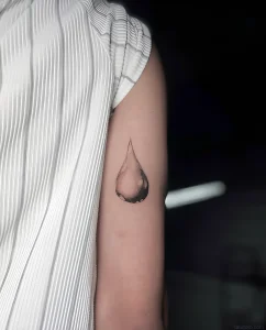 Минималистичная татуировка капли на плече, выполненная в технике blackwork с реалистичной передачей объема и бликов.
