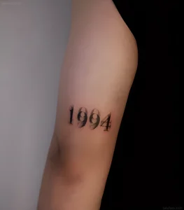 Минималистичная татуировка на плече с цифрами 1994, выполненная в технике дотворк, символизирующая год рождения.