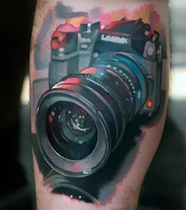 Фотореалистичная татуировка на руке с изображением фотоаппарата Panasonic, выполненная в технике акварели с яркими цветовыми акцентами.