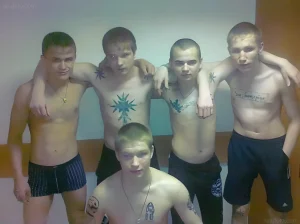 Группа мужчин с татуировками на груди и руках позирует для фотографии. На татуировках изображены звезды, кресты и другие символические элементы, характерные для тюремной татуировки.
