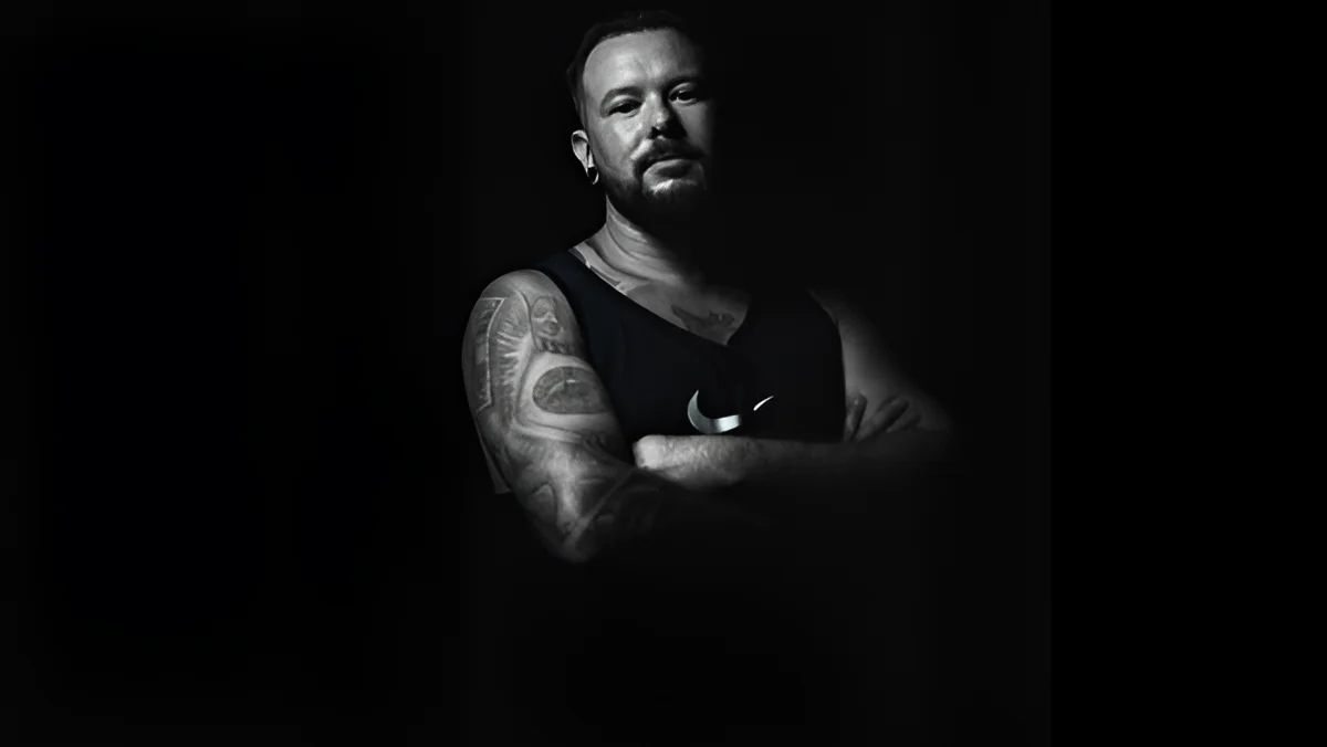 Томас Келлингер, основатель Thomas K. Tattoo Galerie, на фоне темного фона, демонстрирующий татуировки на руке.