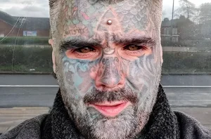 Крупный план лица King Of Ink Land King Body Art The Extreme Ink-Ite, покрытого сложными татуировками.