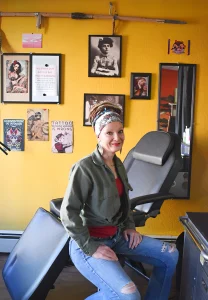 Бри Блё Макки, художник по татуировкам, в своей студии Inkology Tattoo в городе Райфл, штат Колорадо, на фоне портрета Мод Вагнер, первой женщины-тату-мастера в США.