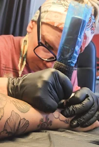 Бри Блё Макки делает татуировку клиенту в Inkology Tattoo в городе Райфл, штат Колорадо. На заднем плане виден портрет Мод Вагнер.