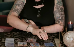 Морган, основательница Inked Goddess Creations, проводит гадание на Таро, демонстрируя татуировки на рукавах.